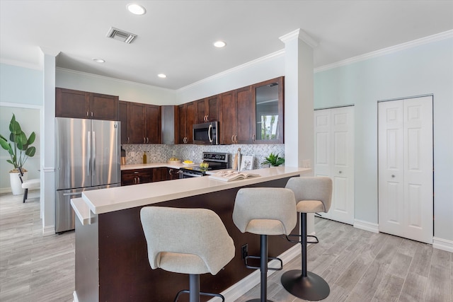kitchen with stainless steel appliances, a kitchen breakfast bar, light countertops, dark brown cabinetry, and recessed lighting