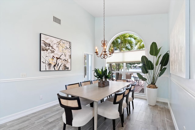 dining room featuring a chandelier, light wood-style flooring, baseboards, and a high ceiling