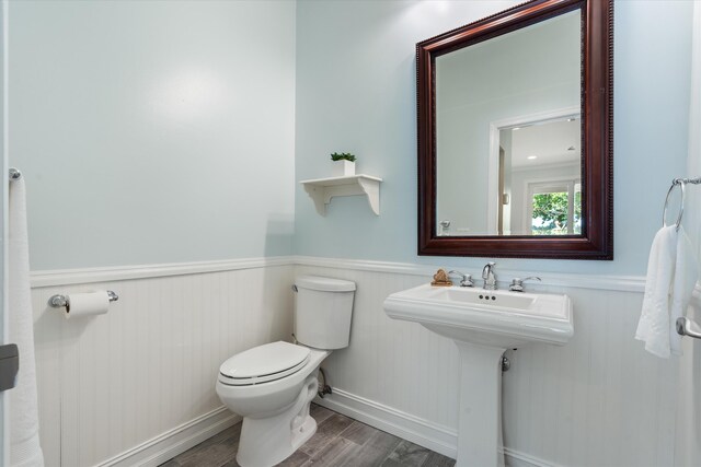 half bathroom featuring toilet, wood finished floors, wainscoting, and a sink