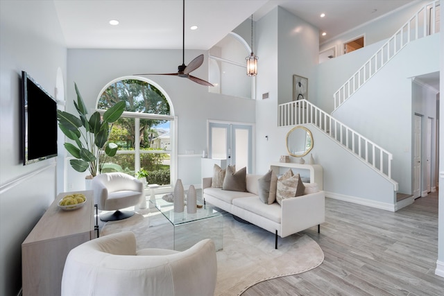 living area featuring a ceiling fan, wood finished floors, stairway, a high ceiling, and french doors