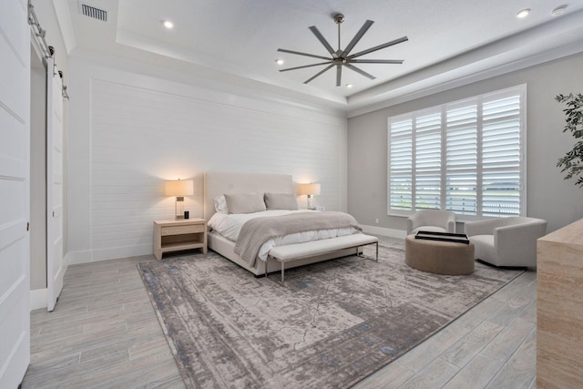 bedroom featuring a barn door, light wood-style floors, a raised ceiling, baseboards, and recessed lighting