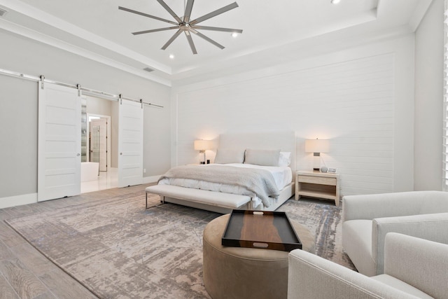 bedroom with a barn door, wood finished floors, a tray ceiling, baseboards, and recessed lighting