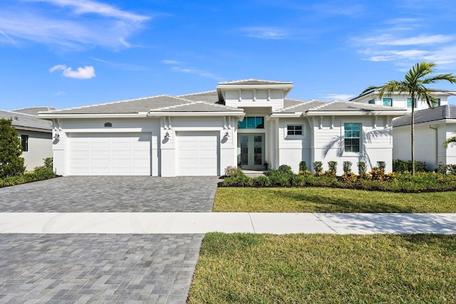 prairie-style house featuring french doors, an attached garage, decorative driveway, a front yard, and a tile roof