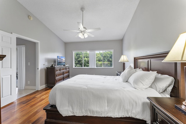 bedroom with vaulted ceiling, wood finished floors, a textured ceiling, ceiling fan, and baseboards