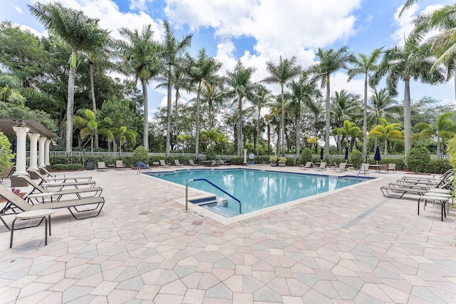 community pool with a patio, fence, and view of scattered trees
