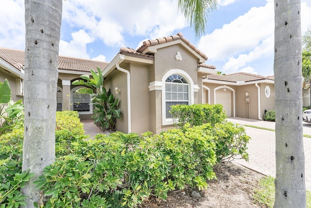 mediterranean / spanish home with a tiled roof, stucco siding, an attached garage, and driveway