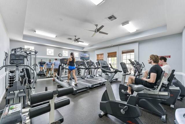 exercise room featuring a textured ceiling, a tray ceiling, and ceiling fan