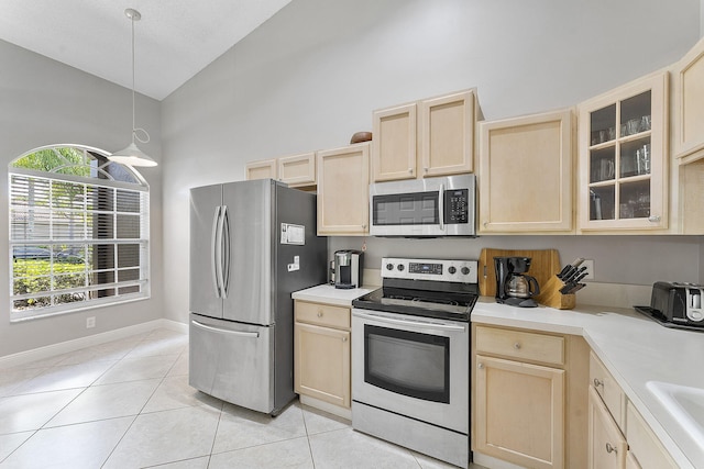 kitchen with stainless steel appliances, light brown cabinetry, light tile patterned floors, light countertops, and high vaulted ceiling