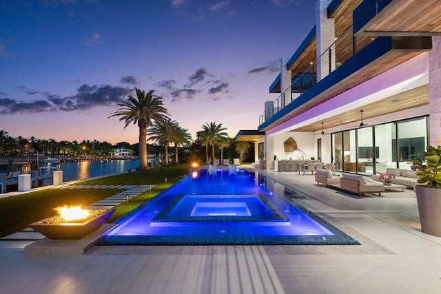 4460 NE 31st Ave, Lighthouse Point, FL 33064 - pool at dusk featuring an outdoor living space with a fire pit, a patio area, a water view, and a pool with connected hot tub