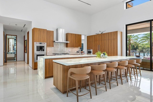 4460 NE 31st Ave, Lighthouse Point, FL 33064 - kitchen with wall chimney exhaust hood, modern cabinets, a spacious island, brown cabinets, and a high ceiling