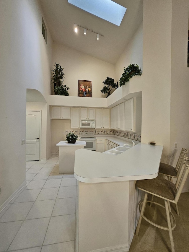 1639 SW Harbour Isles Cir Unit 29, Port Saint Lucie, FL 34986 - kitchen featuring white appliances, a skylight, a peninsula, high vaulted ceiling, and rail lighting