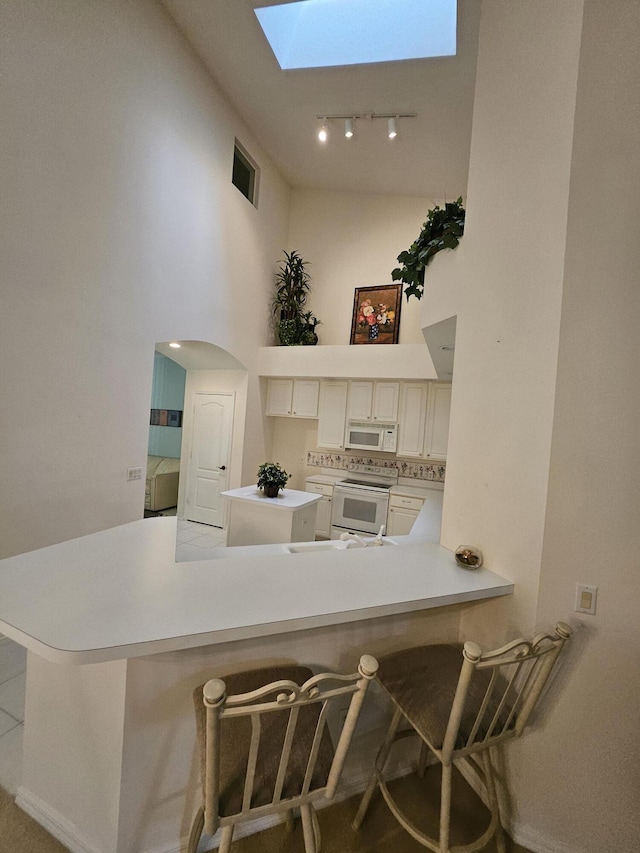 1639 SW Harbour Isles Cir Unit 29, Port Saint Lucie, FL 34986 - kitchen featuring white appliances, a skylight, rail lighting, light countertops, and a towering ceiling