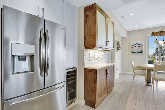 kitchen featuring stainless steel fridge with ice dispenser, light countertops, wine cooler, decorative backsplash, and recessed lighting