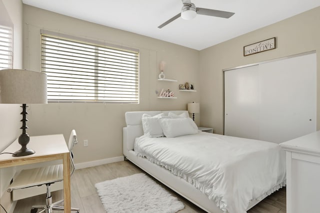 bedroom with light wood-type flooring, a desk, a closet, baseboards, and ceiling fan