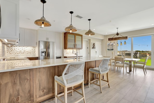 kitchen with stainless steel fridge, light countertops, decorative backsplash, glass insert cabinets, and recessed lighting