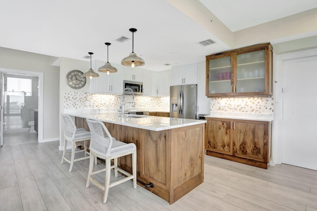 kitchen featuring stainless steel appliances, a kitchen bar, glass insert cabinets, light countertops, and a peninsula