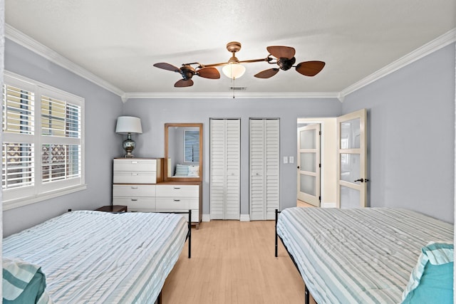 bedroom featuring ornamental molding, light wood-style flooring, a ceiling fan, and two closets