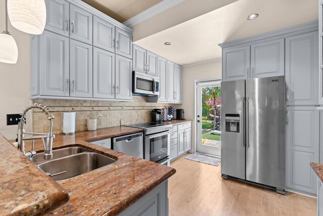 kitchen with appliances with stainless steel finishes, a sink, tasteful backsplash, crown molding, and light wood finished floors