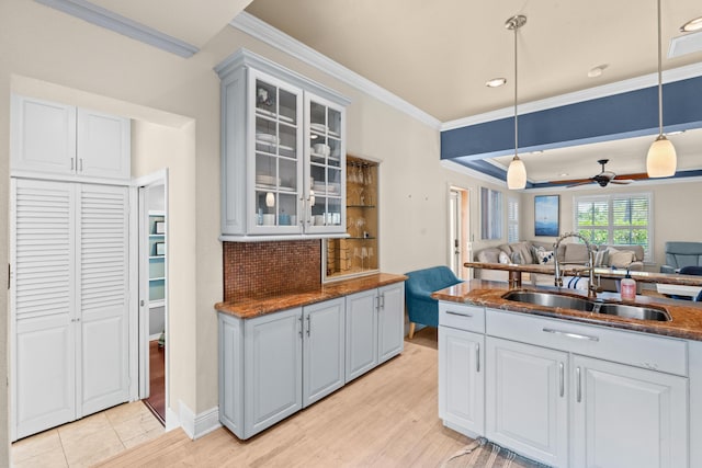 kitchen with a sink, open floor plan, crown molding, decorative light fixtures, and glass insert cabinets
