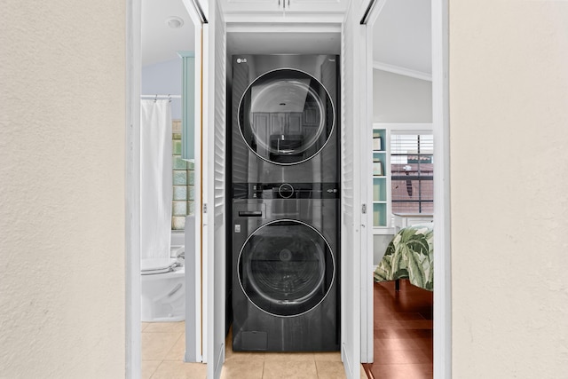 clothes washing area featuring stacked washer / drying machine, light tile patterned floors, a textured wall, and ornamental molding