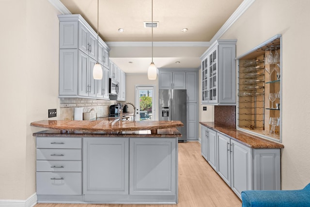 kitchen featuring stainless steel appliances, decorative backsplash, a peninsula, ornamental molding, and light wood finished floors