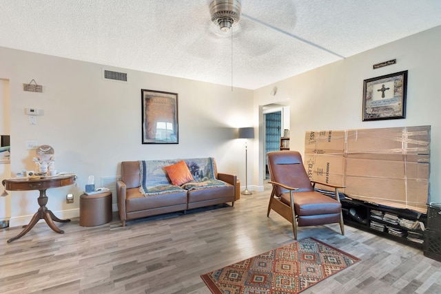 living room featuring wood finished floors, a textured ceiling, a ceiling fan, and baseboards