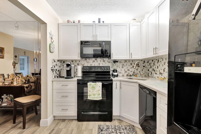 kitchen featuring black appliances, a sink, light wood-style floors, backsplash, and white cabinets