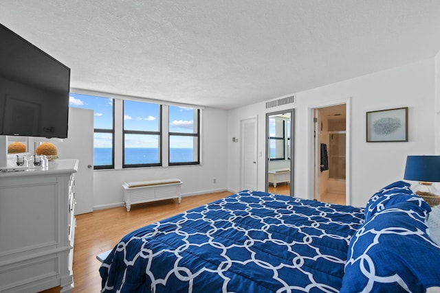 bedroom with a textured ceiling, light wood-type flooring, ensuite bathroom, and baseboards