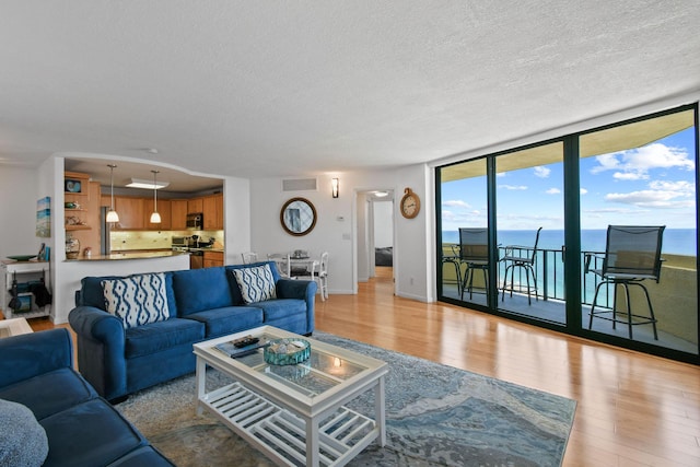 living area with light wood-style floors, a textured ceiling, a water view, baseboards, and expansive windows