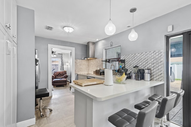 8611 NW 47th Ct, Lauderhill, FL 33319 - kitchen with wall chimney exhaust hood, a kitchen breakfast bar, tasteful backsplash, white cabinets, and a peninsula