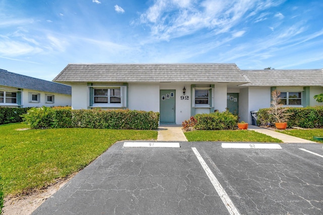 view of front of house with mansard roof, stucco siding, uncovered parking, and a front yard