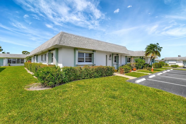 view of front of home featuring mansard roof, uncovered parking, stucco siding, and a front yard