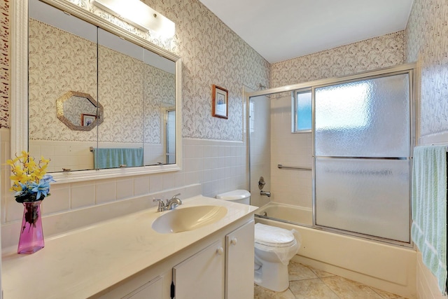 bathroom featuring wallpapered walls, toilet, wainscoting, vanity, and shower / bath combination with glass door
