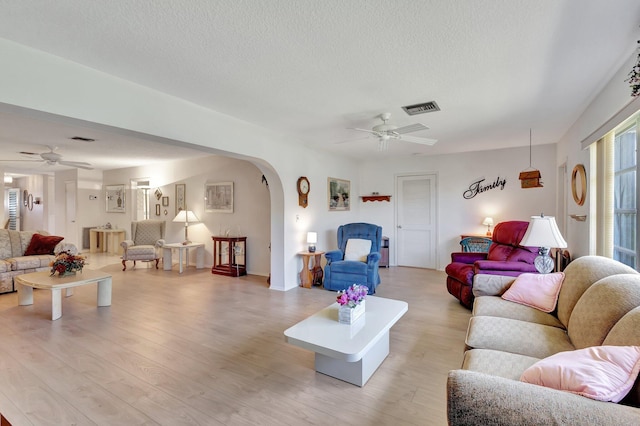 living room with ceiling fan, arched walkways, light wood finished floors, and a textured ceiling