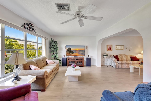 living area featuring arched walkways, a textured ceiling, a ceiling fan, and light wood-style floors