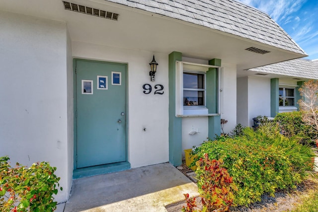 entrance to property with stucco siding and roof with shingles