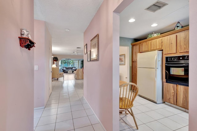kitchen featuring freestanding refrigerator, black oven, light tile patterned flooring, and baseboards