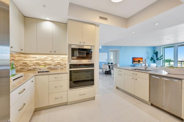 kitchen with appliances with stainless steel finishes, a sink, open floor plan, light countertops, and backsplash