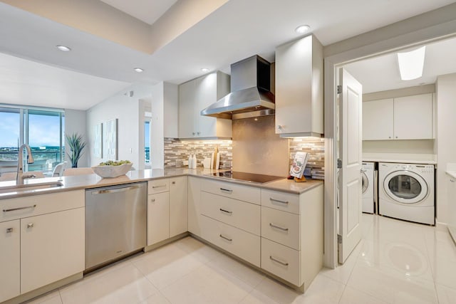 kitchen with stainless steel dishwasher, wall chimney range hood, washing machine and dryer, a sink, and black electric cooktop