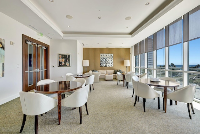 dining space with light colored carpet, a tray ceiling, a water view, and french doors