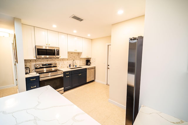 kitchen with stainless steel appliances, a sink, white cabinets, tasteful backsplash, and dark cabinetry