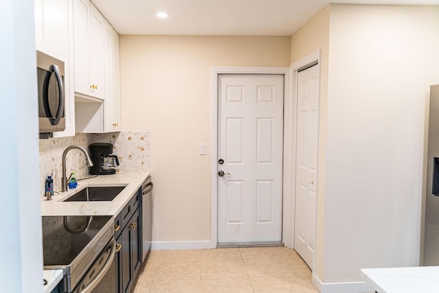 kitchen featuring appliances with stainless steel finishes, a sink, white cabinetry, baseboards, and light tile patterned floors