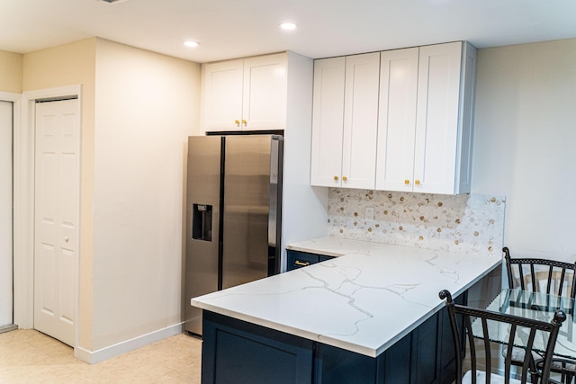 kitchen with stainless steel fridge, light stone countertops, decorative backsplash, white cabinetry, and a peninsula