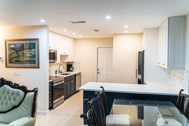 kitchen with stainless steel appliances, white cabinets, light stone countertops, a sink, and decorative backsplash