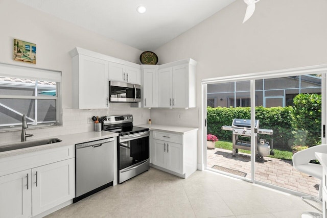 kitchen with stainless steel appliances, a sink, backsplash, light countertops, and lofted ceiling