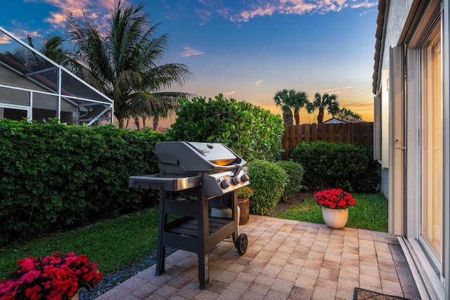 patio terrace at dusk with a lanai, fence, and area for grilling