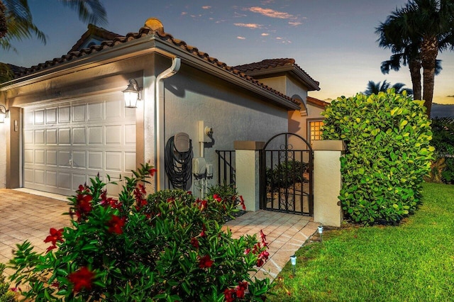 view of home's exterior with a garage, stucco siding, a gate, a tile roof, and driveway