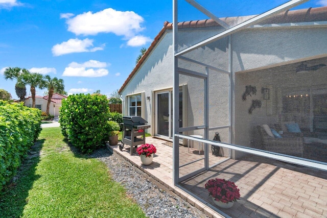 rear view of house featuring stucco siding, a patio, glass enclosure, a lawn, and a tiled roof