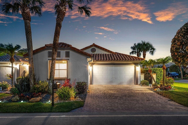 mediterranean / spanish-style house featuring a garage, stucco siding, decorative driveway, and a tiled roof