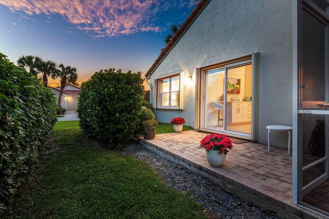 yard at dusk featuring a patio area and a lawn